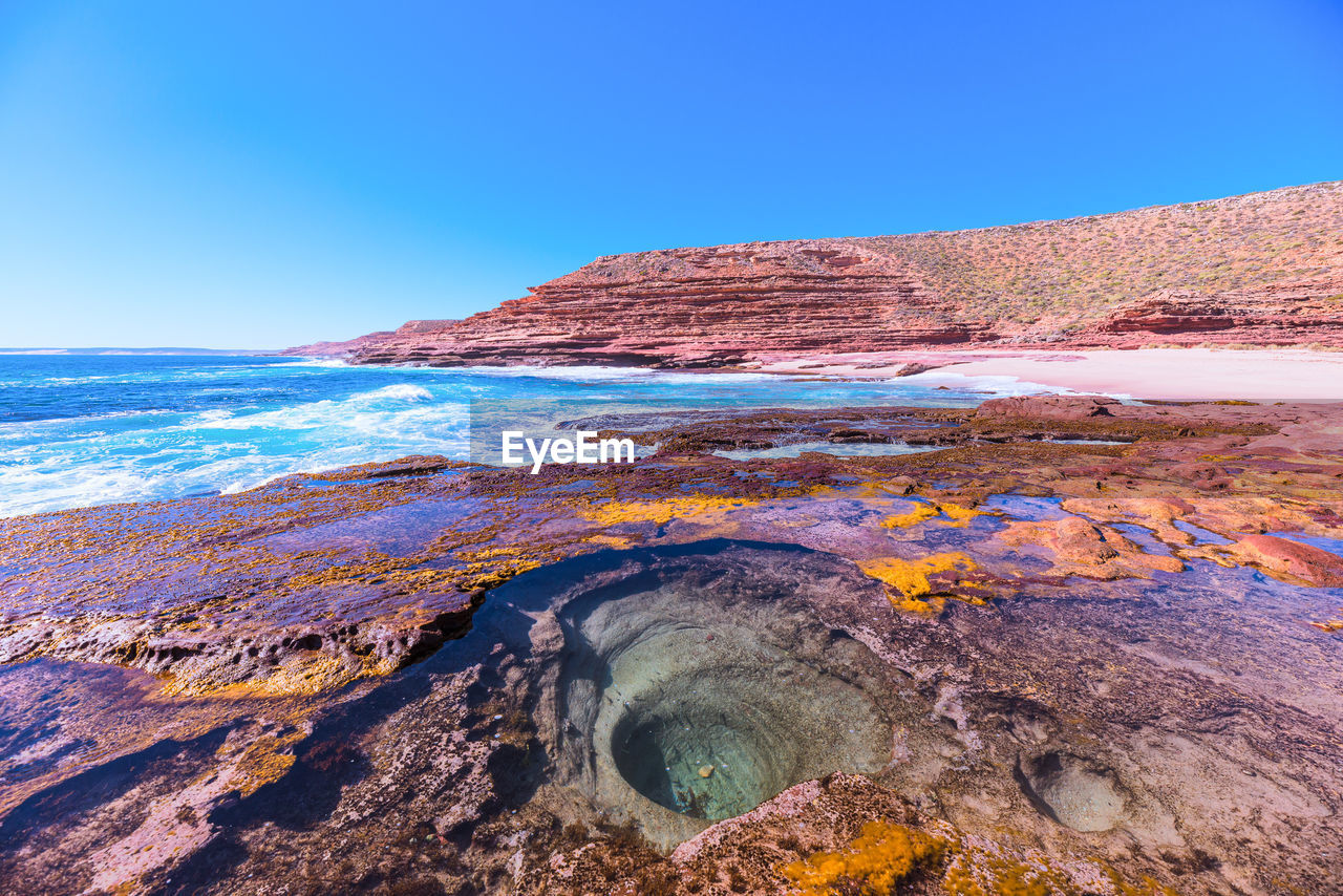 Scenic view of rock formation at sea against clear blue sky