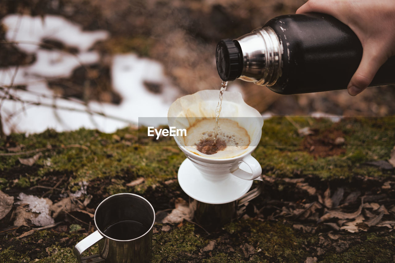 Brewing pour over coffee in nature at a hiking trip. hand pouring hot steaming water into a filter