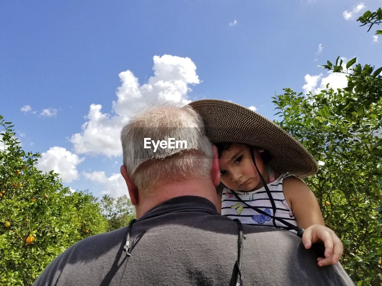 Grandfather carrying daughter against sky