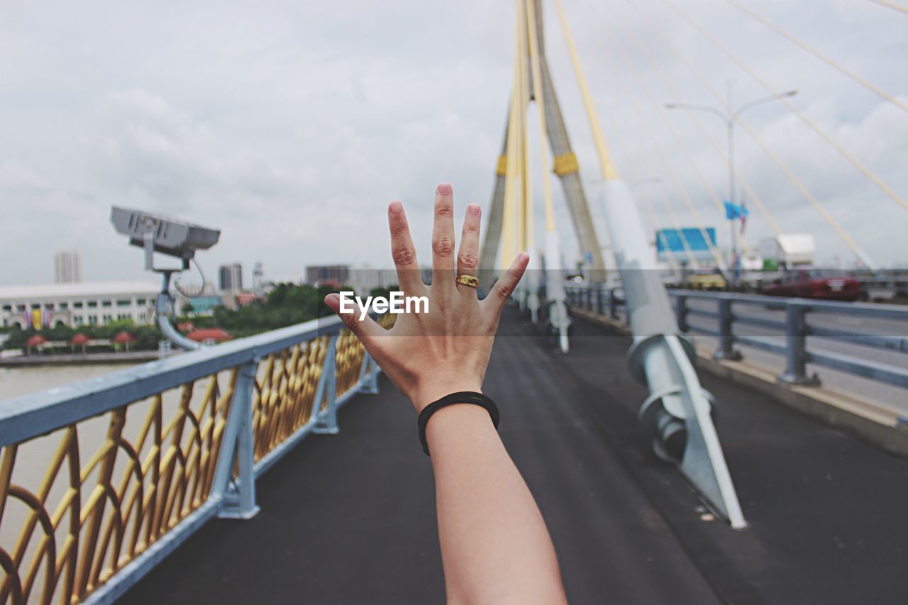 Cropped hand of woman on bridge against sky in city