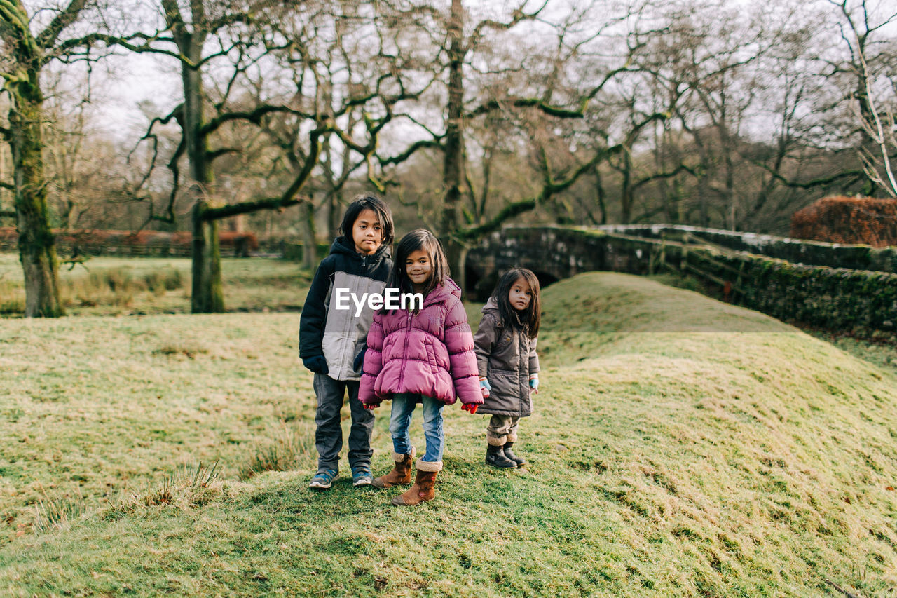 Full length portrait of siblings standing against trees in winter