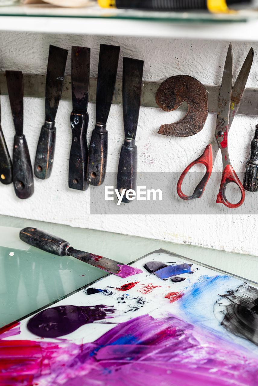 Various chisels and scissors arranged on wall near table with paints on workplace in engraving workshop