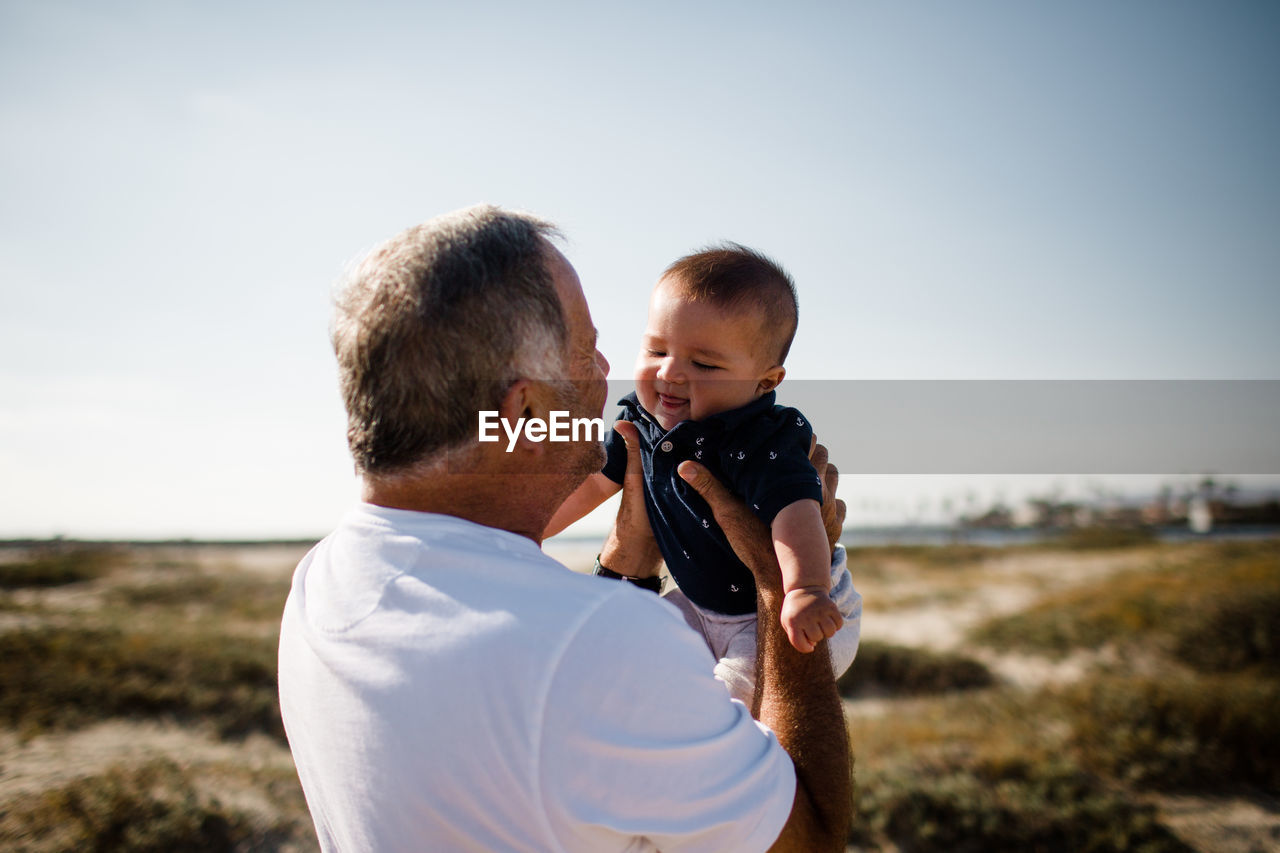 Grandfather holding grandson while standing on beach