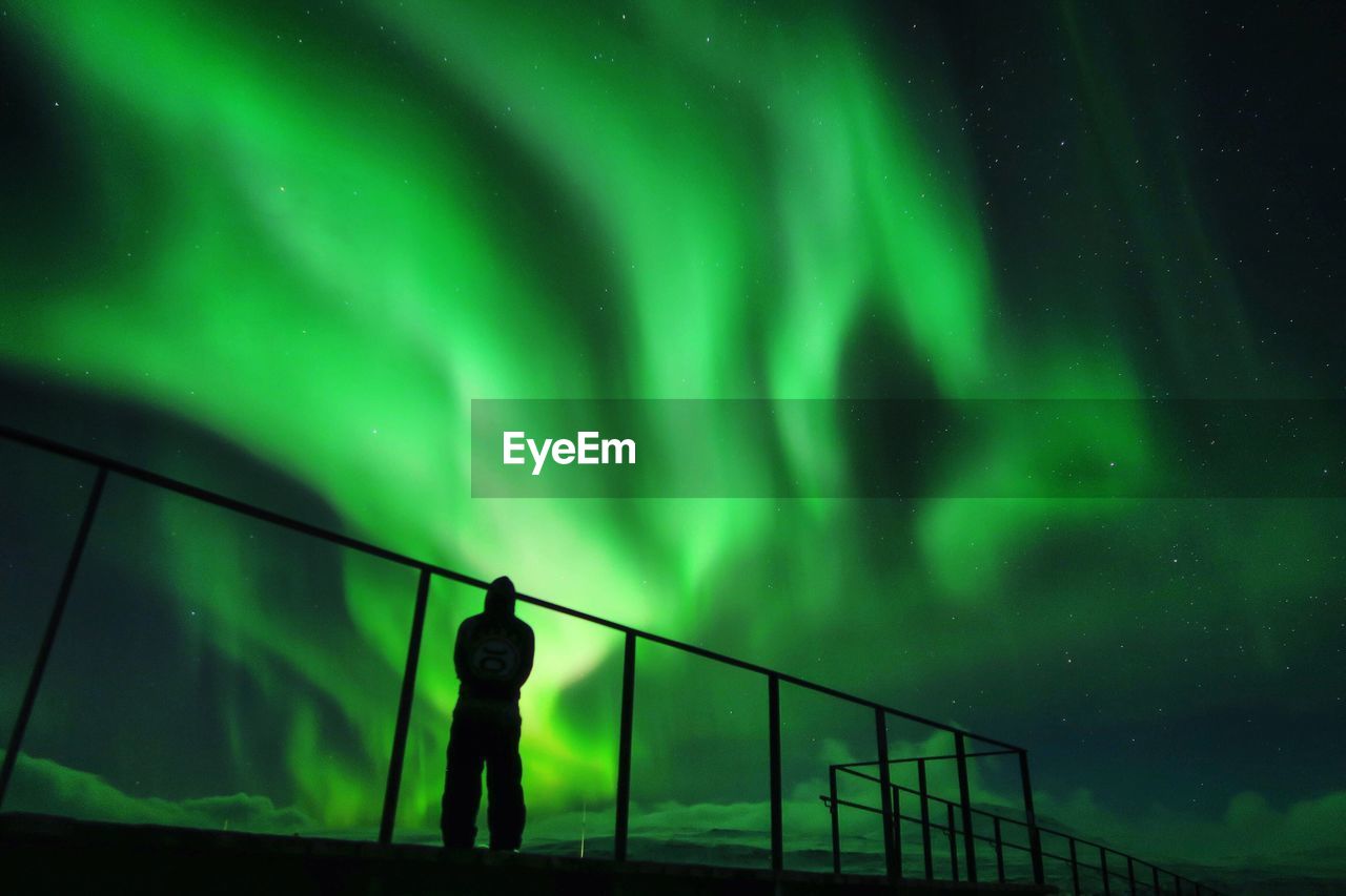 Rear view of man standing against aurora borealis