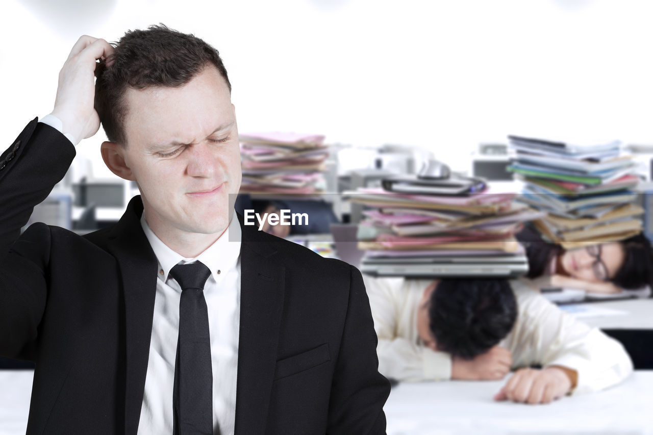 Sad businessman scratching head against tired colleagues