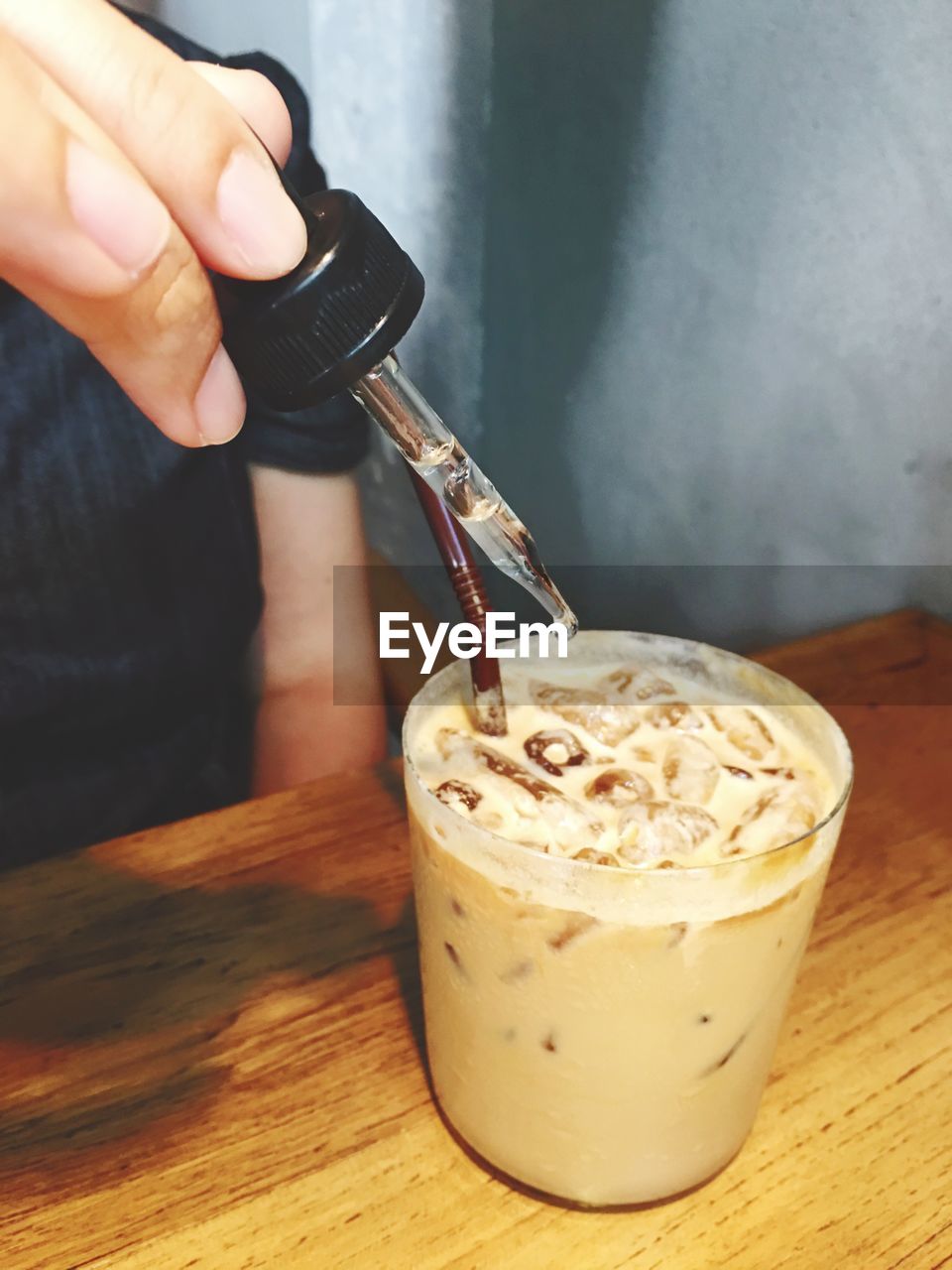 Cropped image of person adding liquid in iced coffee through dropper at restaurant