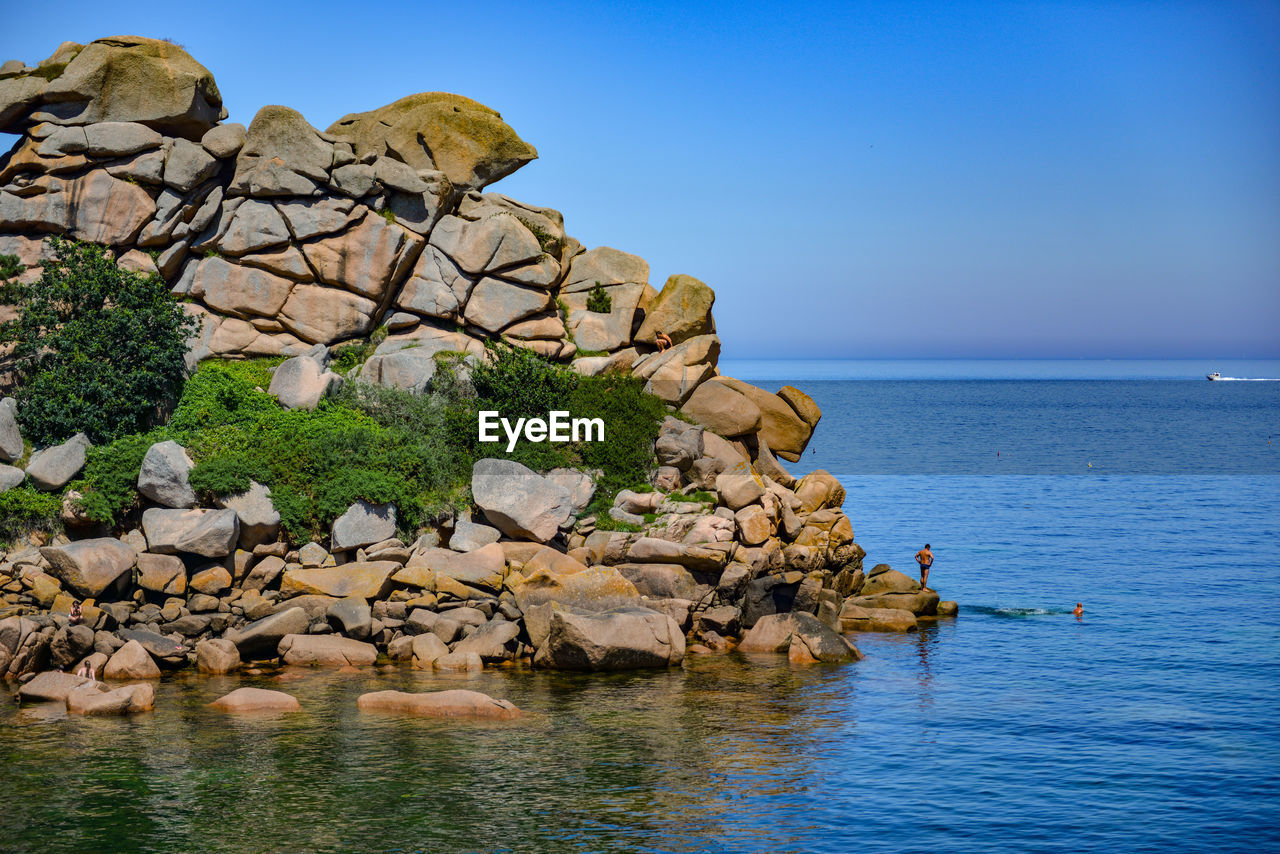 Rock formation by sea against clear sky
