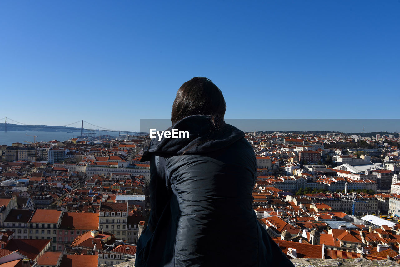 Rear view of woman standing against cityscape against clear blue sky