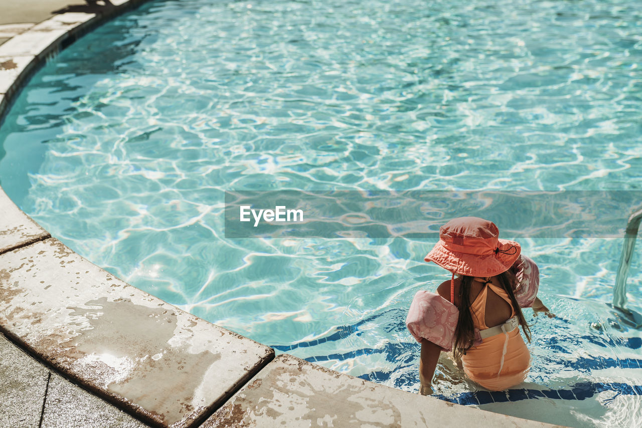 Behind view of little girl swimming in pool on vacation palm springs