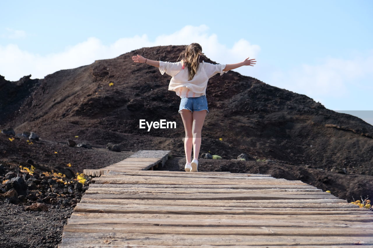 Full length of woman walking on boardwalk against mountain