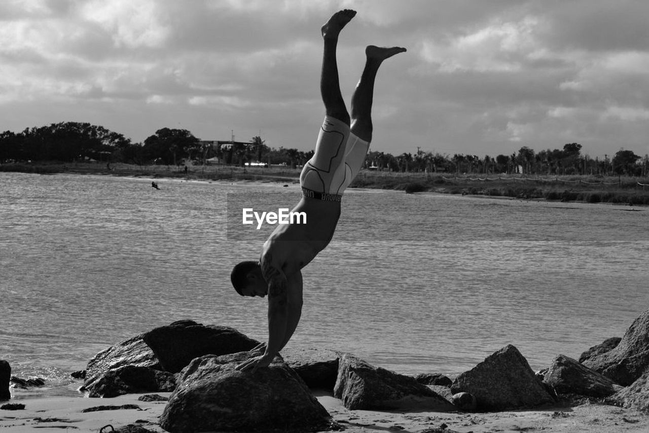 Shirtless young man practicing handstand on rock at beach