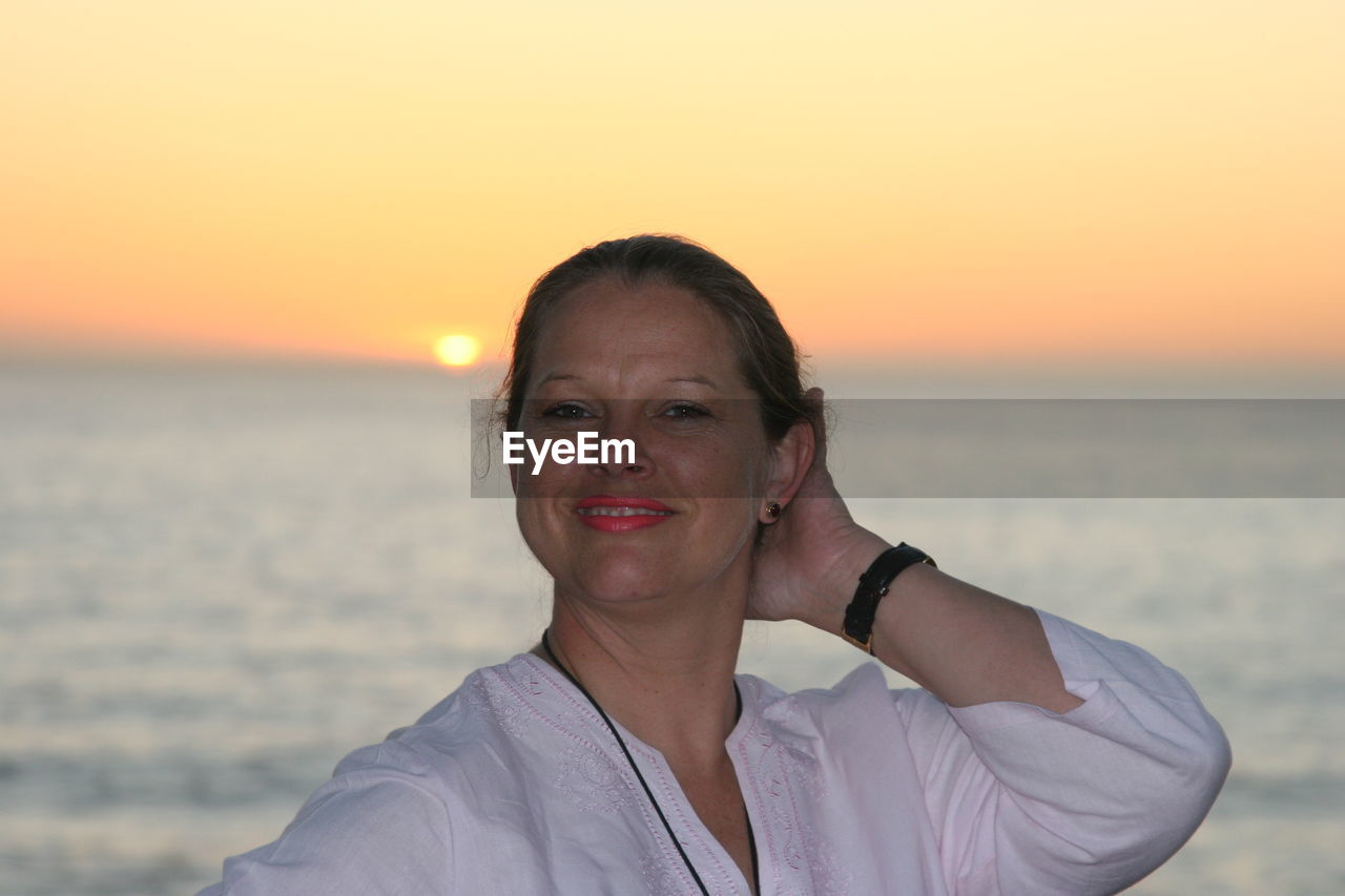 PORTRAIT OF SMILING WOMAN STANDING IN SEA AGAINST SKY