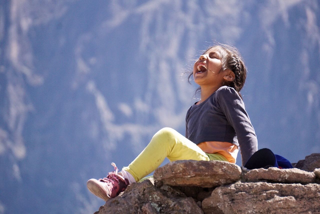 Full length of happy girl sitting on rock