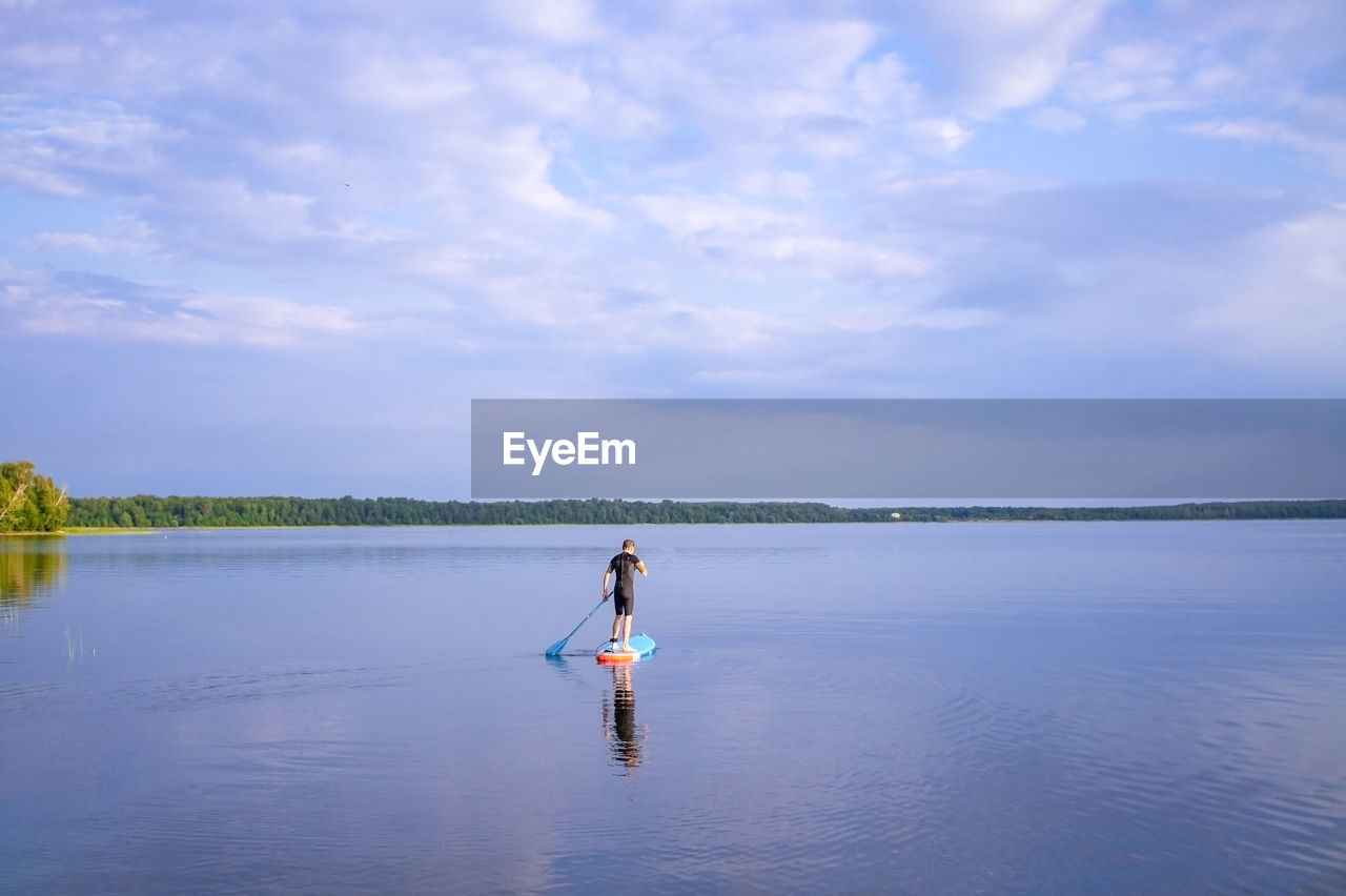 Man is paddling on a sup board on the lake. lake landscape and blue cloudy sky.