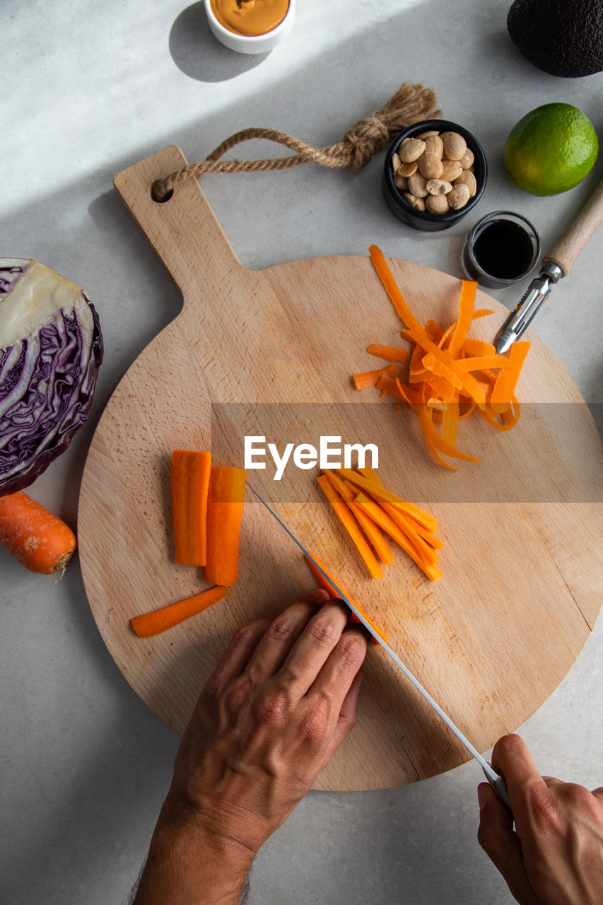 Crop unrecognizable cook chopping fresh carrot on wooden cutting board in kitchen