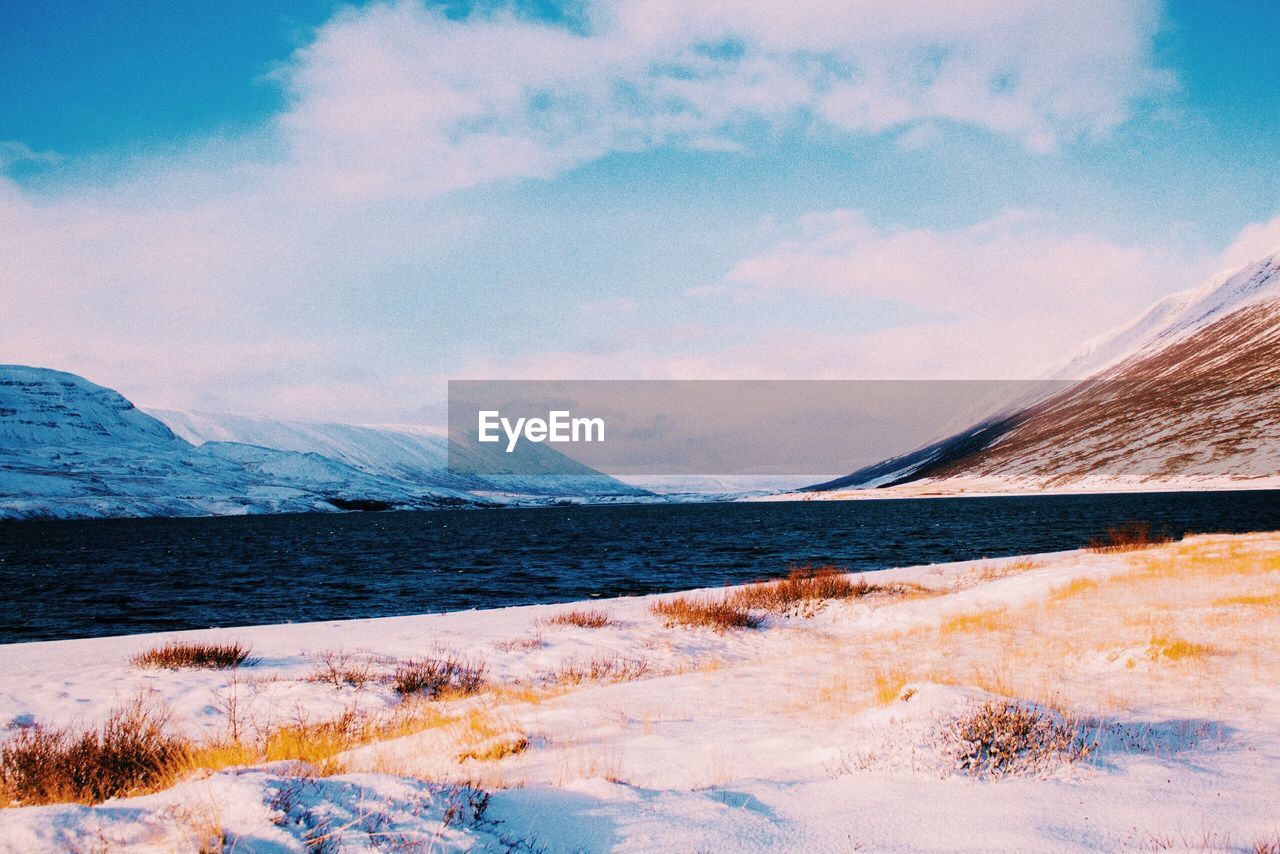 Scenic view of lake by snowcapped mountains against sky