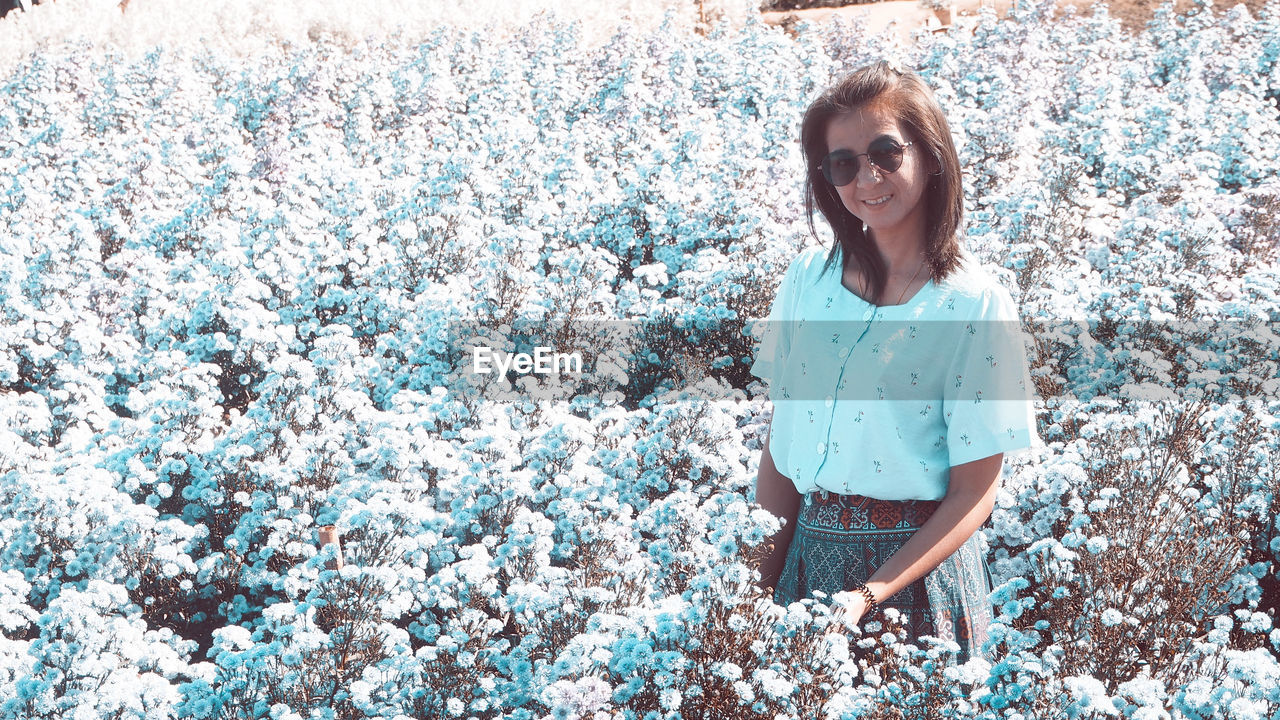 spring, one person, women, blue, casual clothing, standing, flower, front view, day, leisure activity, lifestyles, smiling, nature, portrait, happiness, adult, three quarter length, young adult, looking at camera, emotion, female, plant, person, outdoors, glasses, sunlight, clothing, fashion, land, hairstyle, sunglasses, child, beauty in nature, flowering plant, field, growth, white