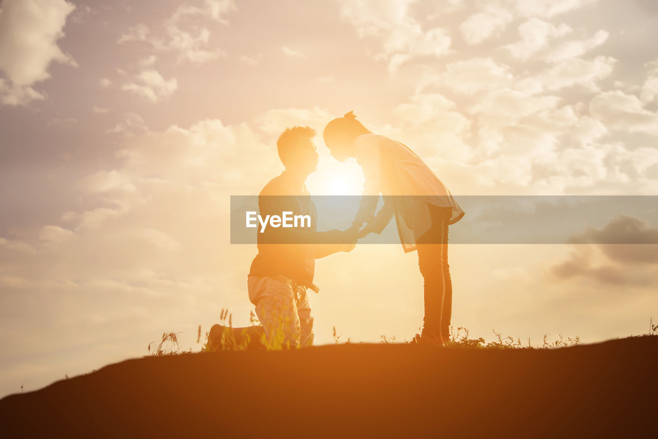 Silhouette couple holding hands against sky during sunset