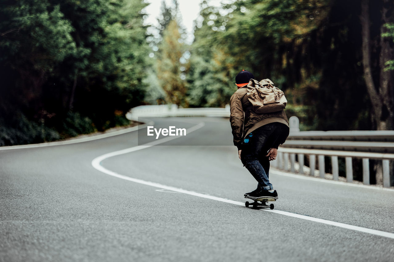 Rear view of man skateboarding on road