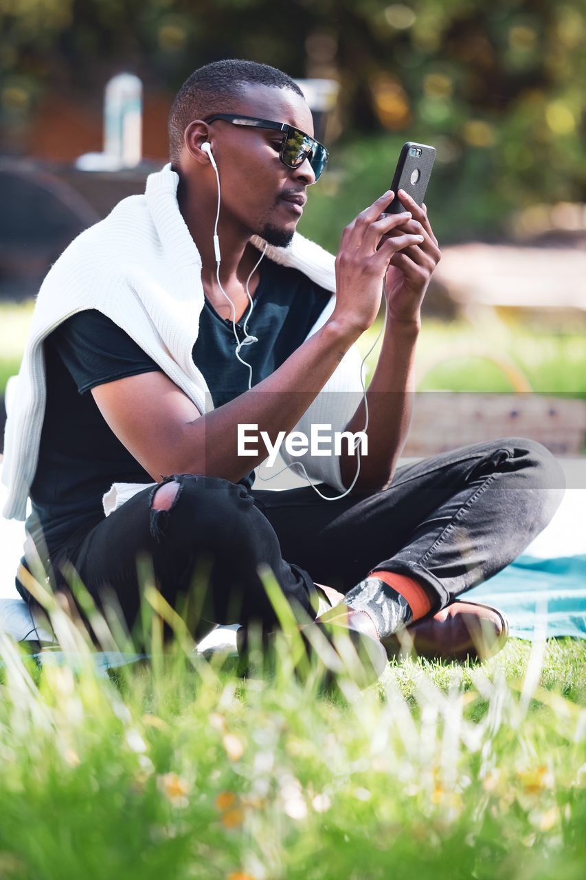 YOUNG MAN USING SMART PHONE SITTING ON GRASS