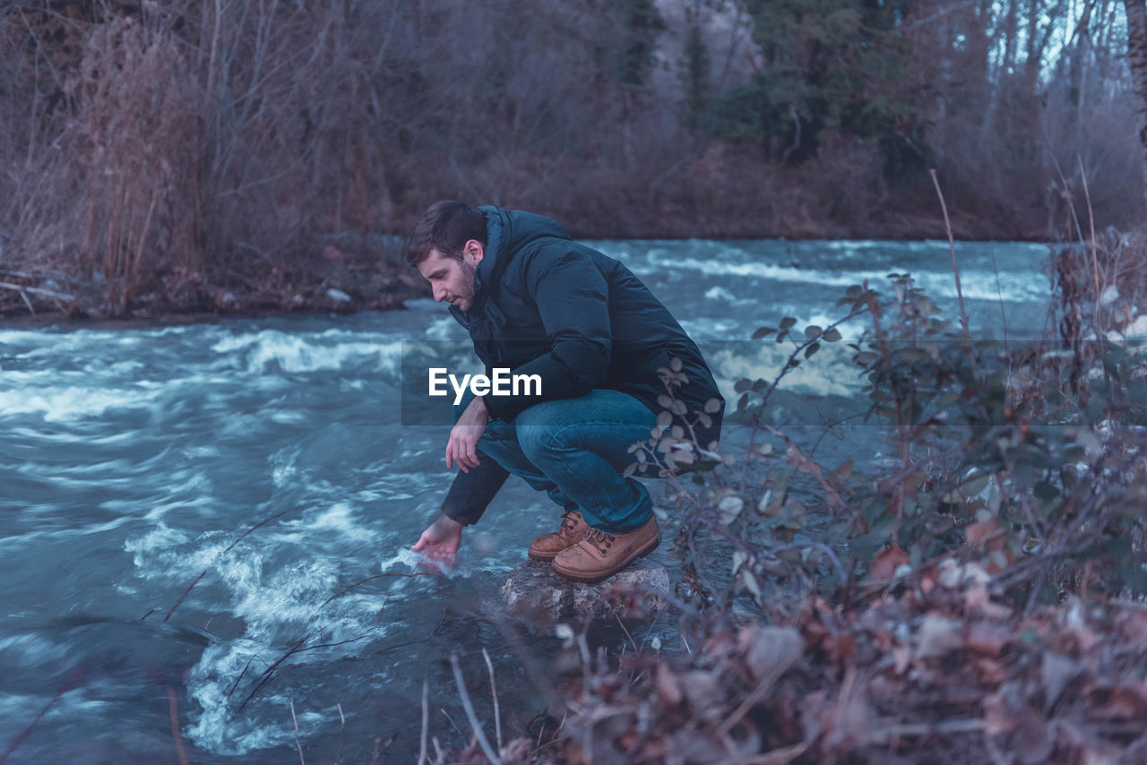 Side view of man with hand in river