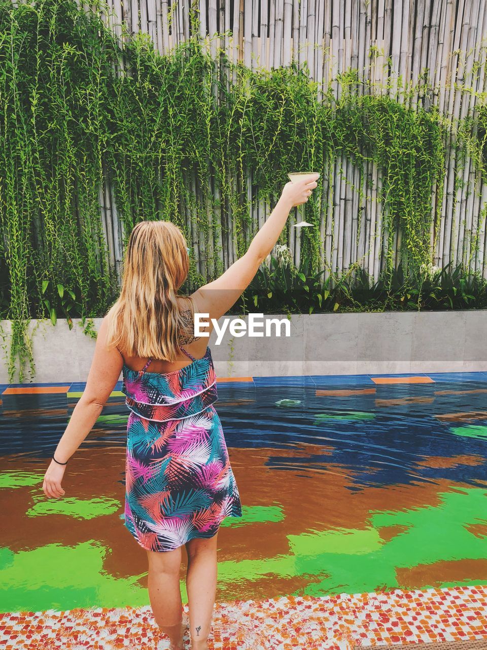 Rear view of woman holding drink standing by pond