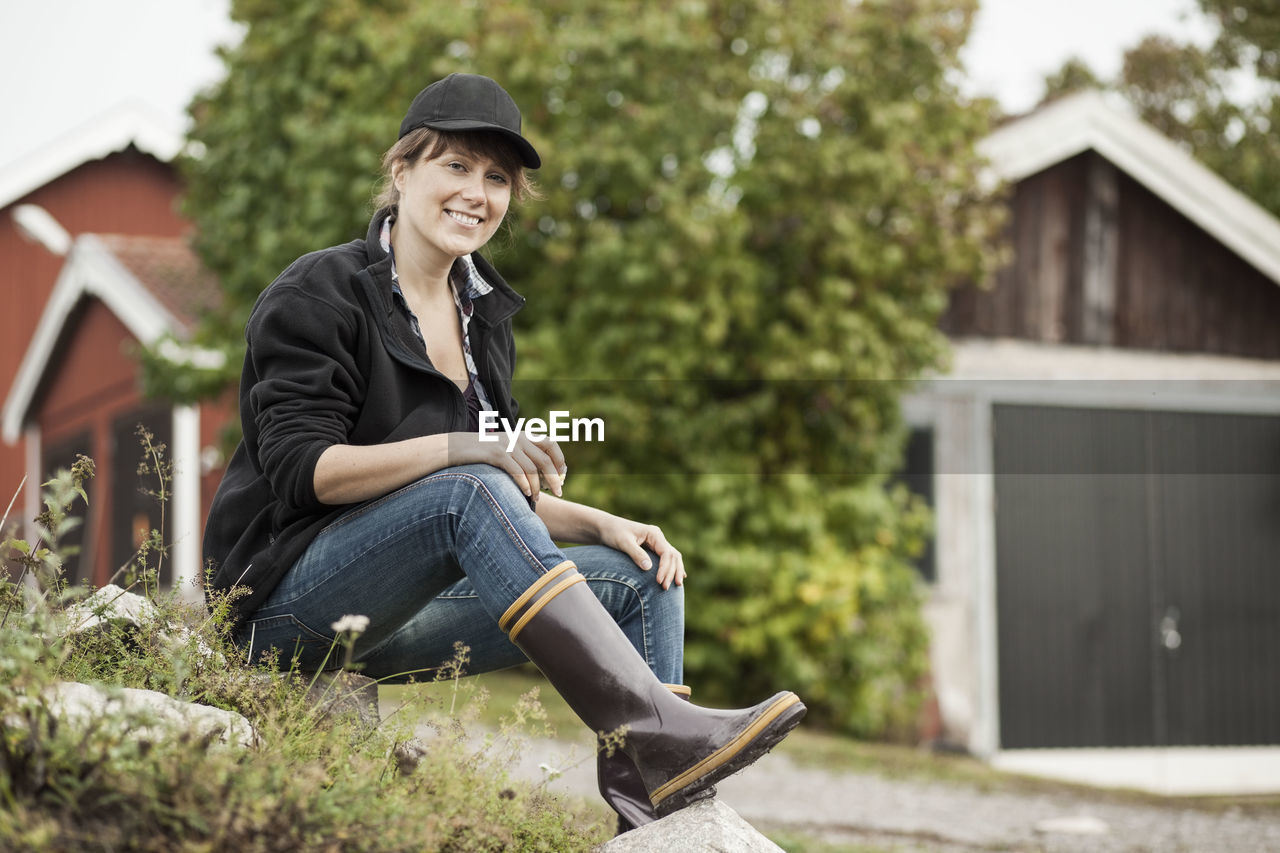 Full length portrait of confident female farmer sitting on rock at farm