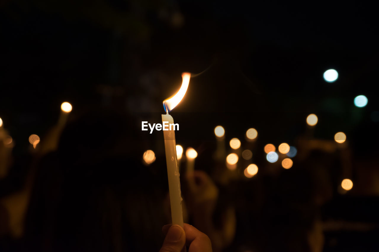 Cropped hand holding illuminated candle at night