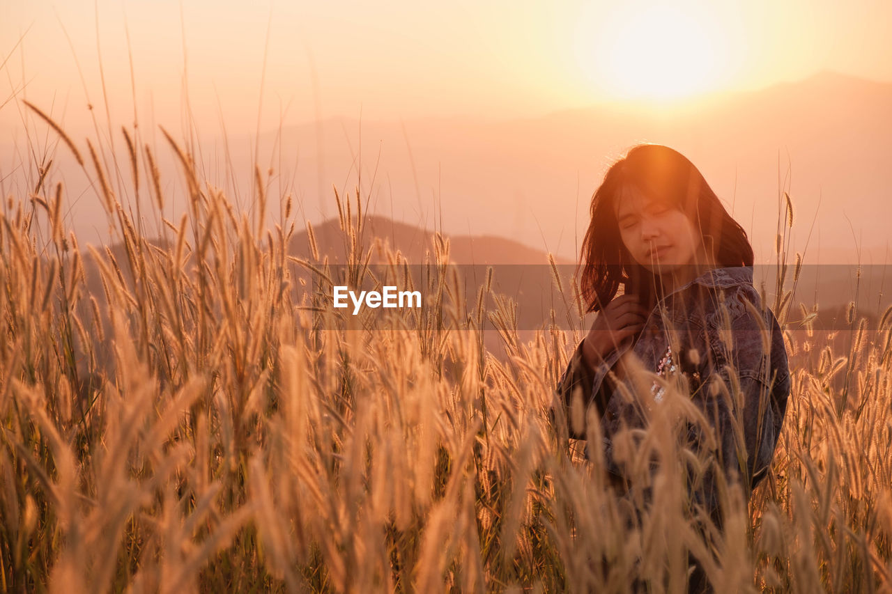 Woman standing on field against sky during sunset