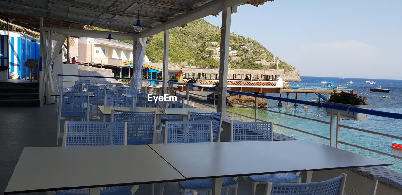 EMPTY CHAIRS BY SWIMMING POOL AGAINST SEA