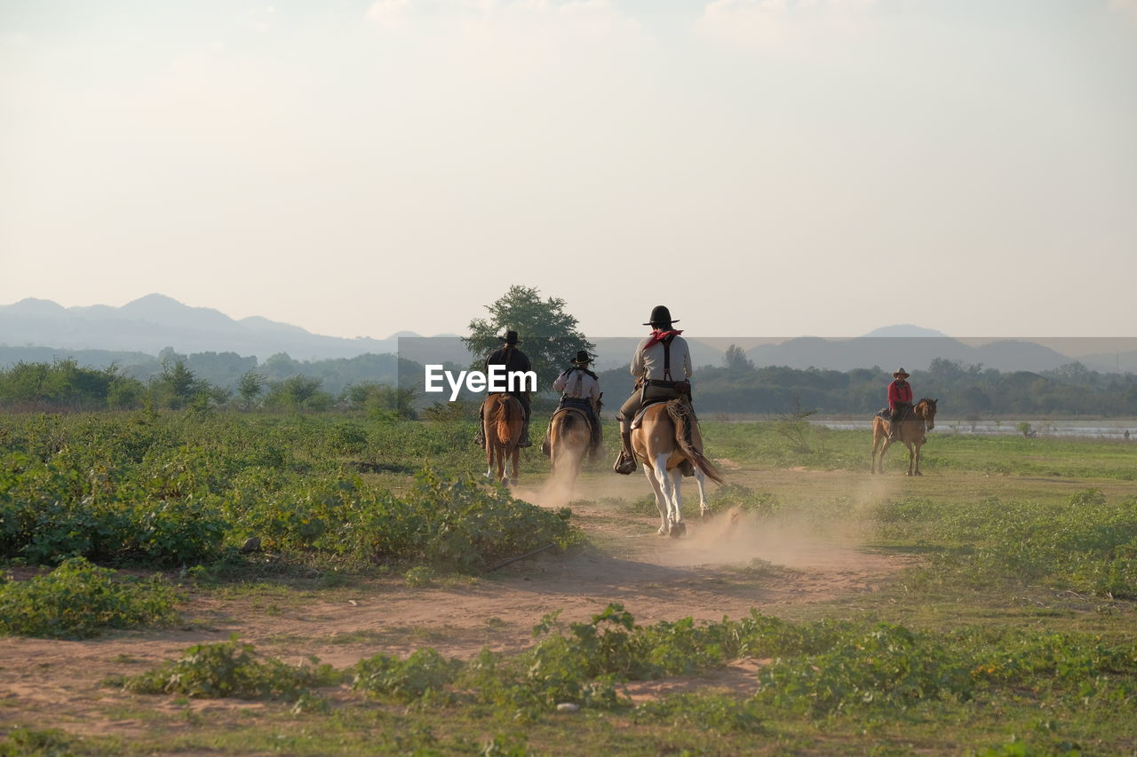 PEOPLE RIDING BICYCLE ON FIELD AGAINST SKY