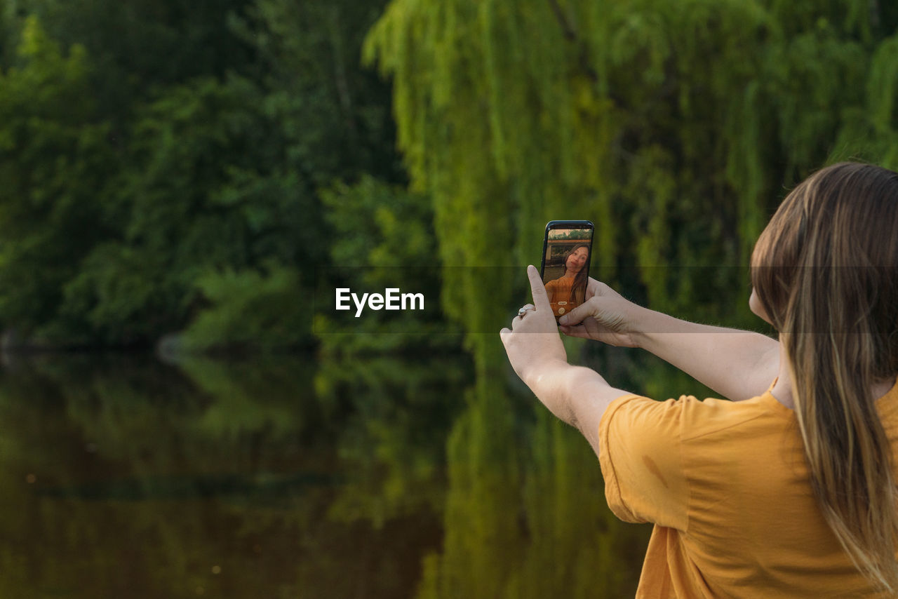 Rear view of woman doing selfie against trees