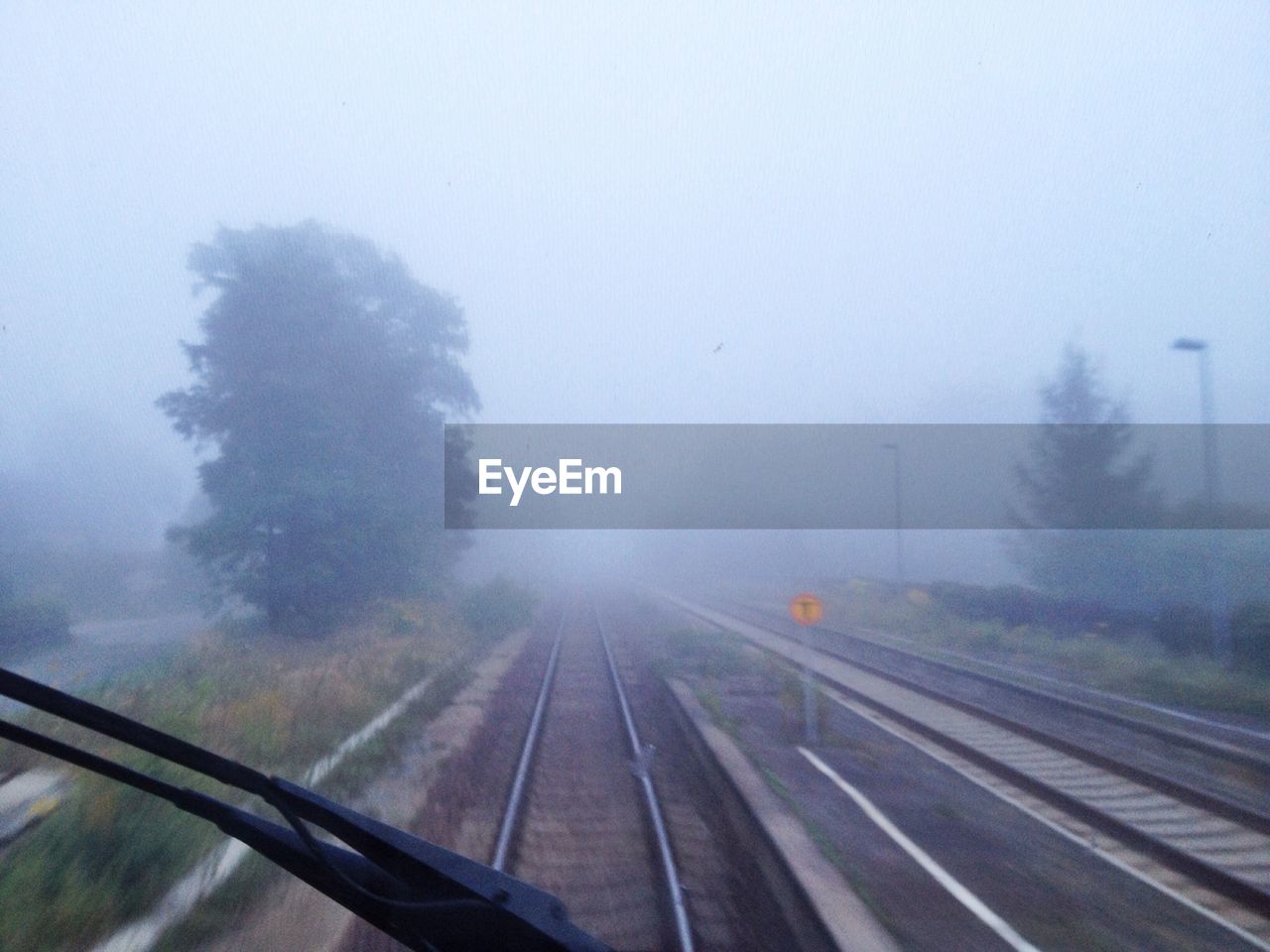 Rail road tracks in foggy weather against clear sky seen through windshield of locomotive