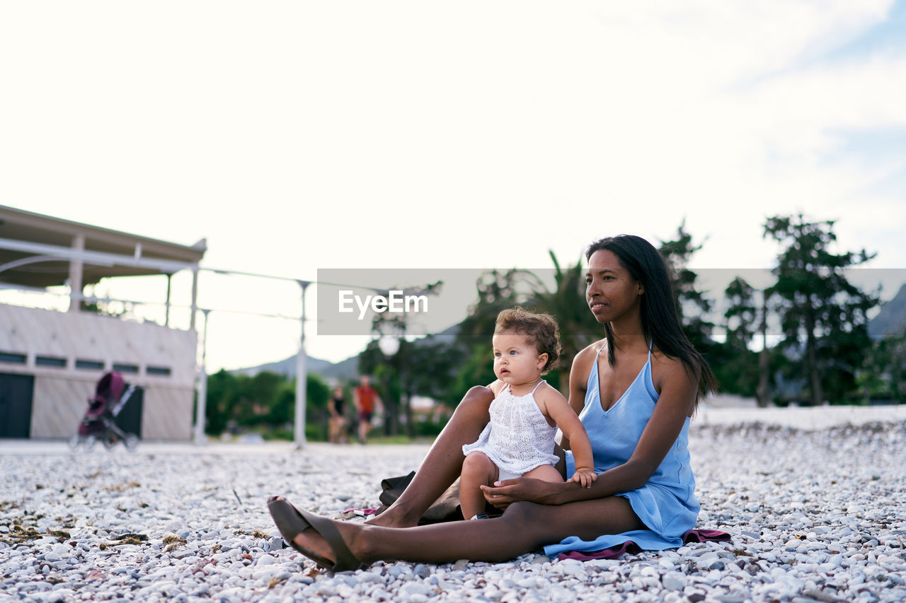 Happy girl sitting on woman against sky