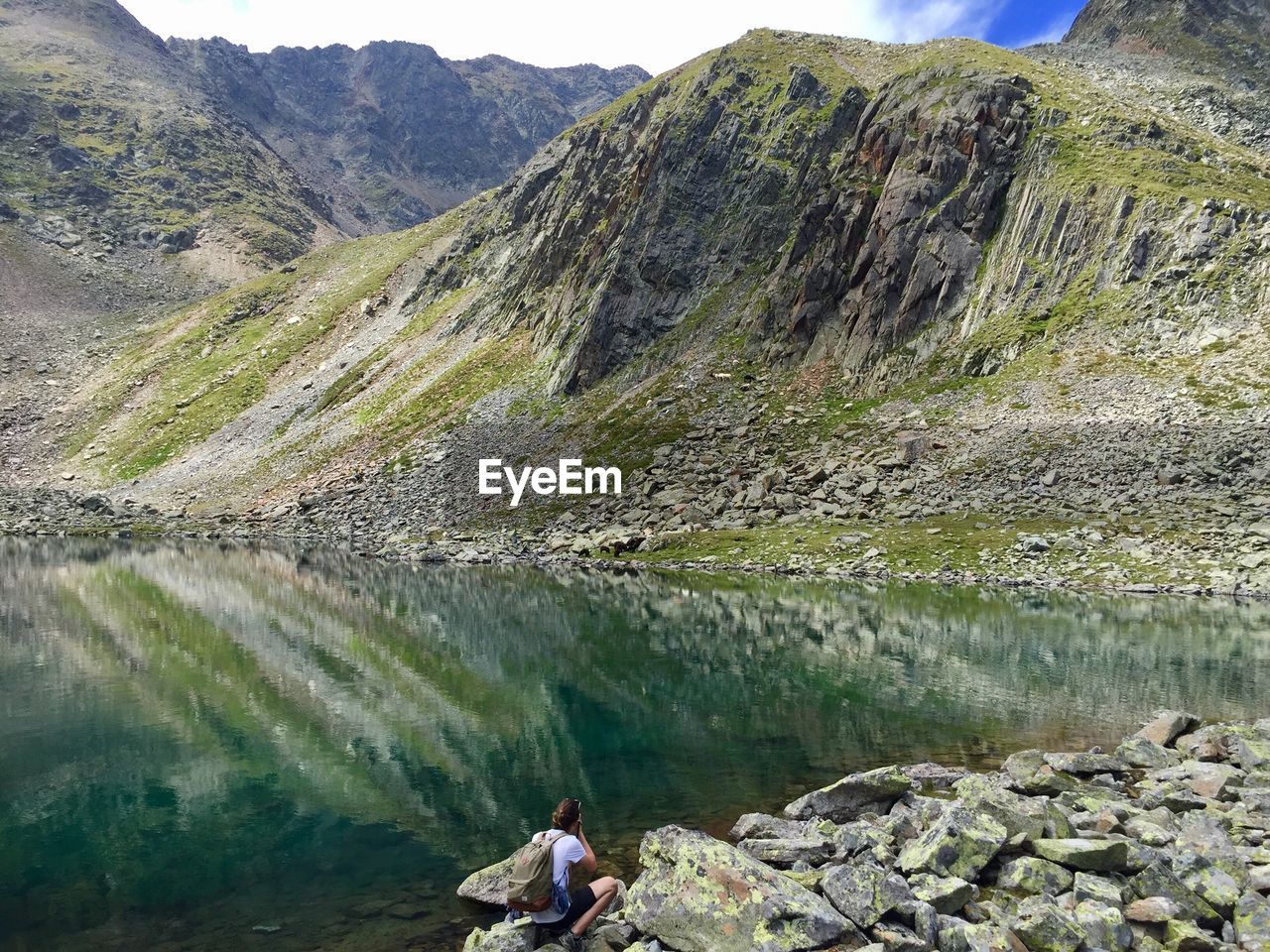 MAN SITTING ON ROCK BY LAKE AGAINST MOUNTAIN