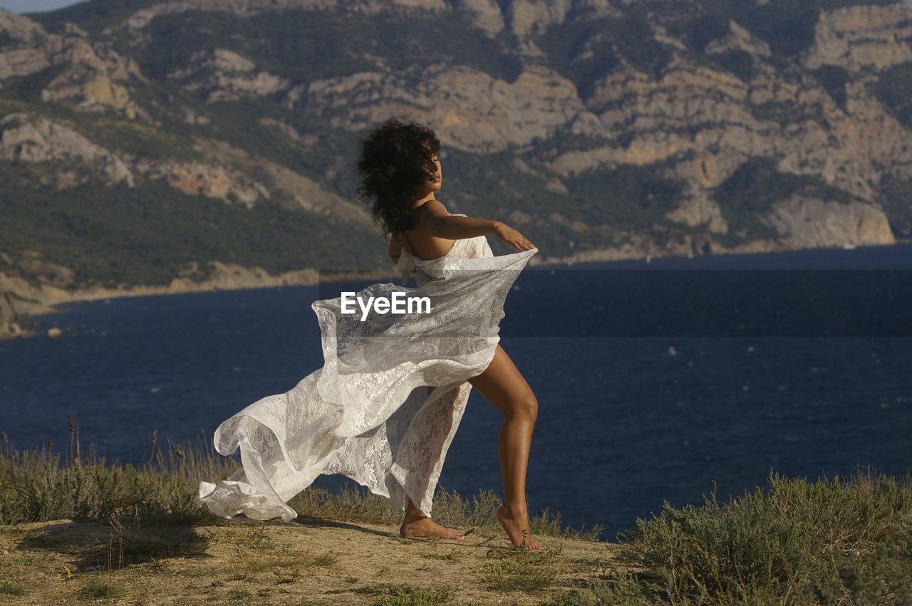Woman in dress posing at lakeshore against mountain