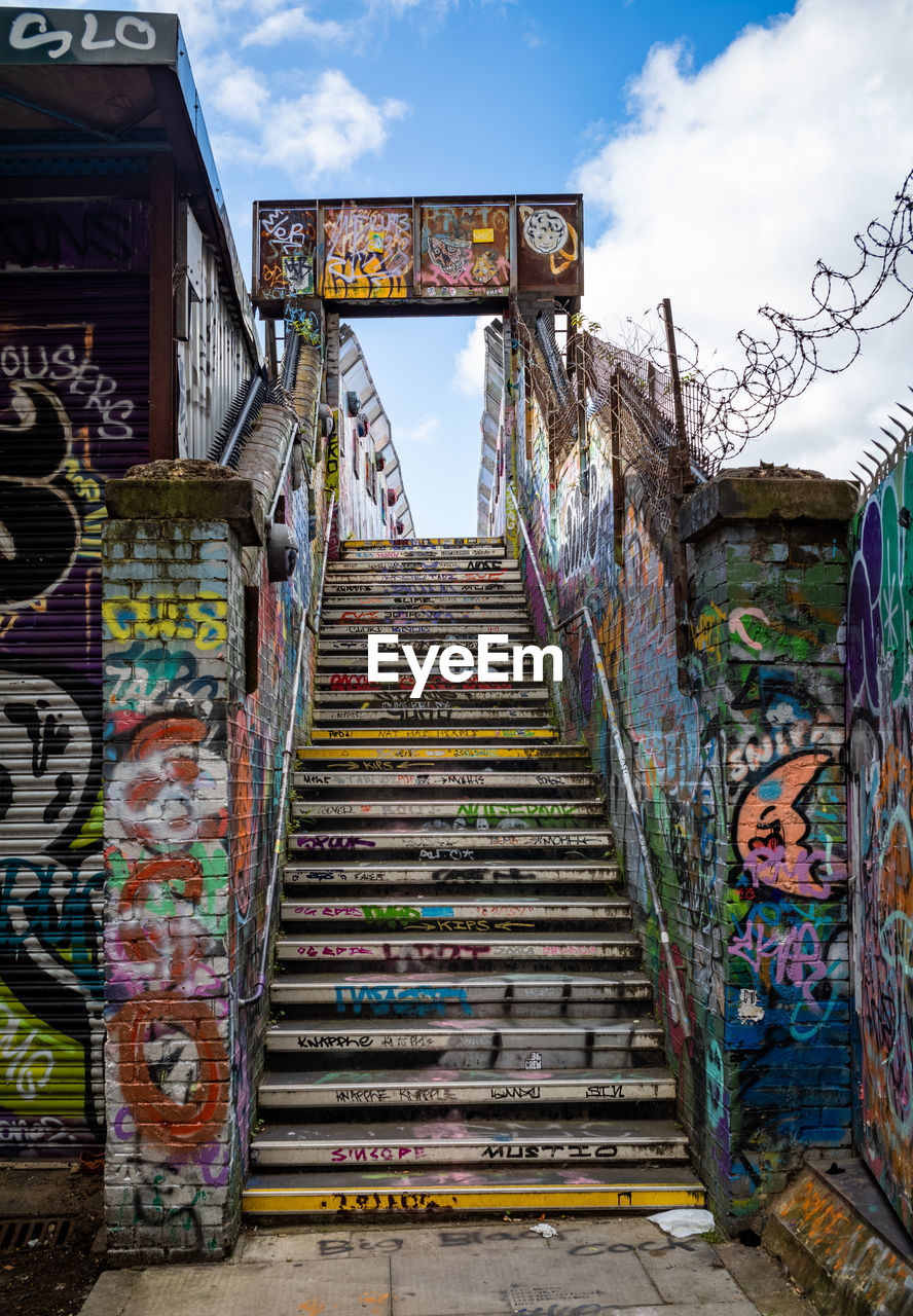 urban area, architecture, staircase, graffiti, sky, art, multi colored, steps and staircases, built structure, cloud, street, no people, street art, day, outdoors, nature, road, building exterior, railing, travel destinations, city, creativity, building, text