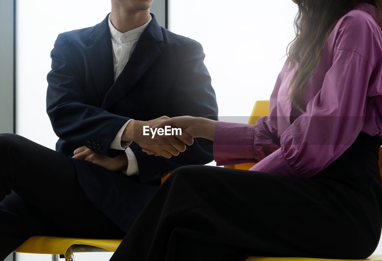 Two people shaking hands in a business setting. the man is wearing a suit and tie, while the woman