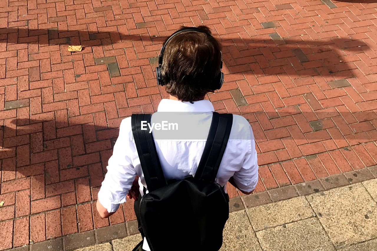 REAR VIEW OF MAN STANDING ON COBBLESTONE