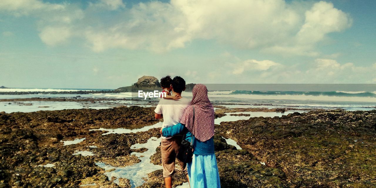 Rear view of family at beach against sky