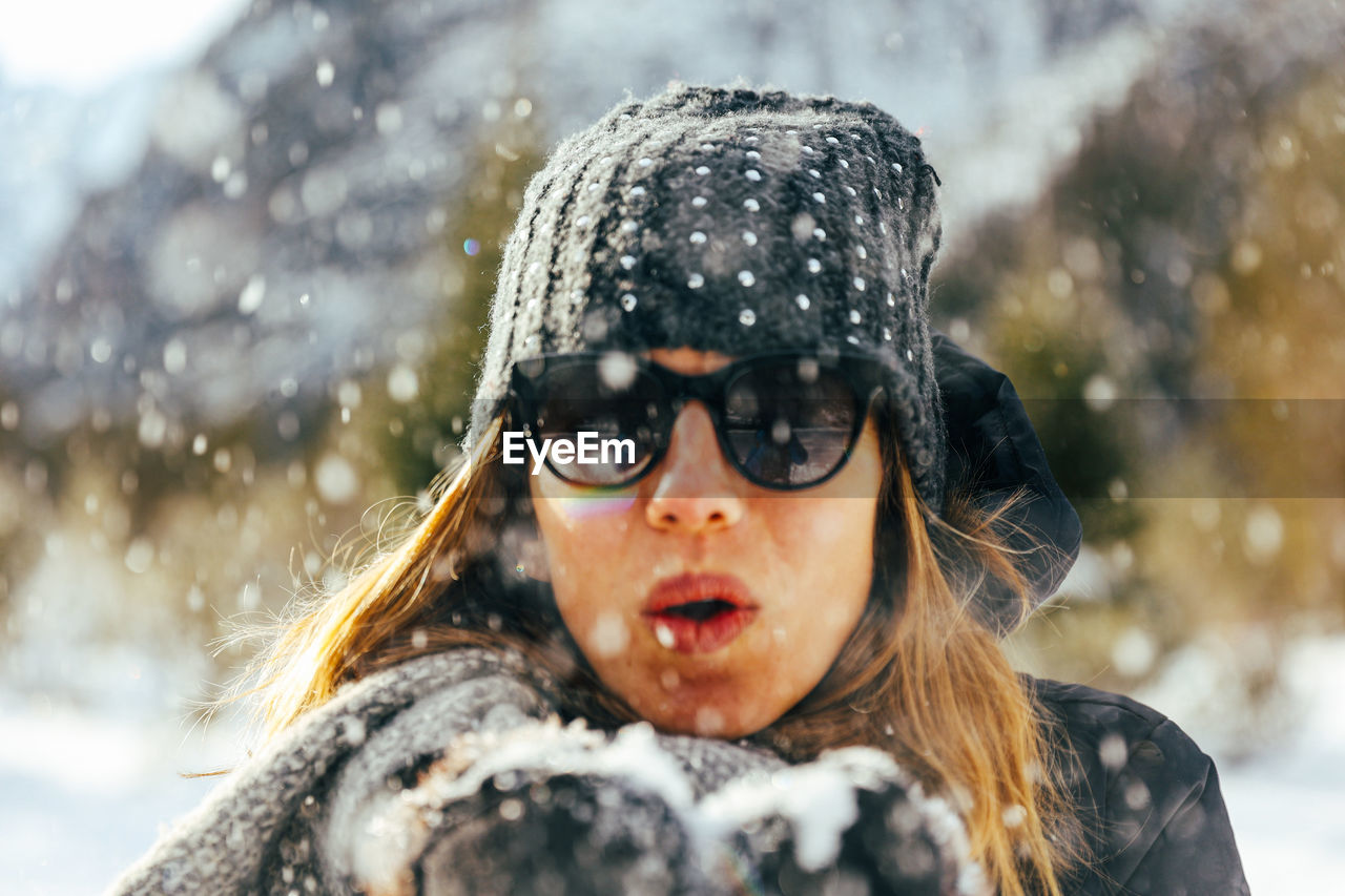 Solo female blowing snow in camera in europe with winter hat and black sunglasses on