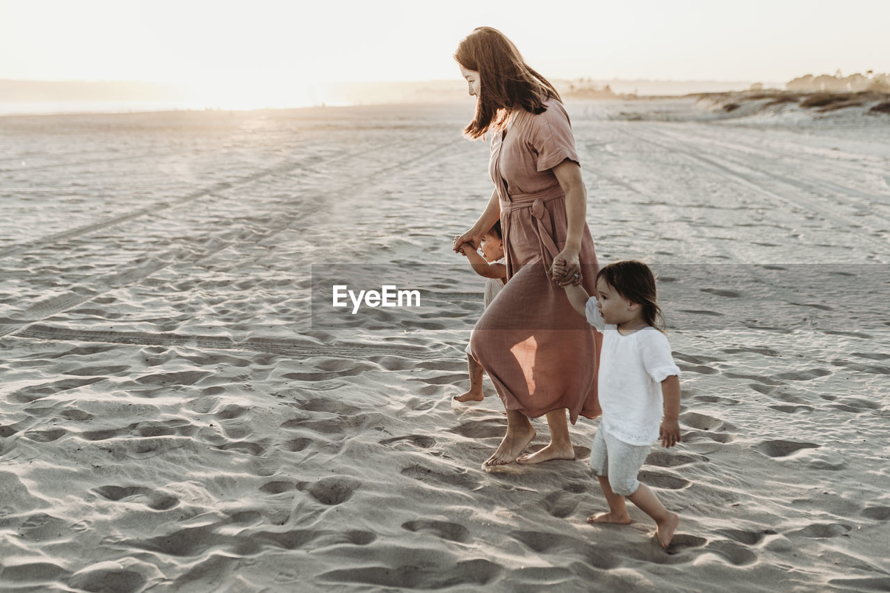 Side view of mother walking toddler twins to ocean with sun setting