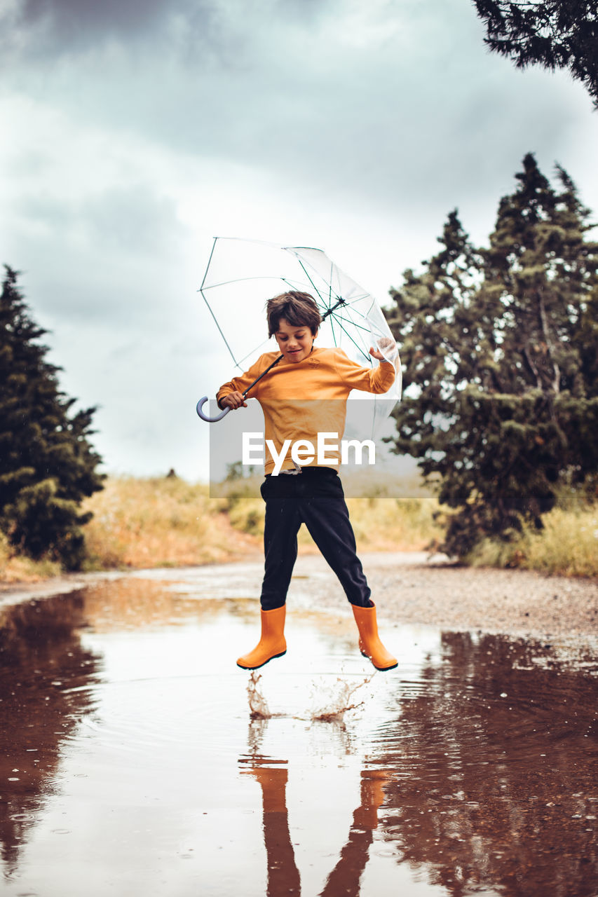 Full length of boy standing on wet glass against sky