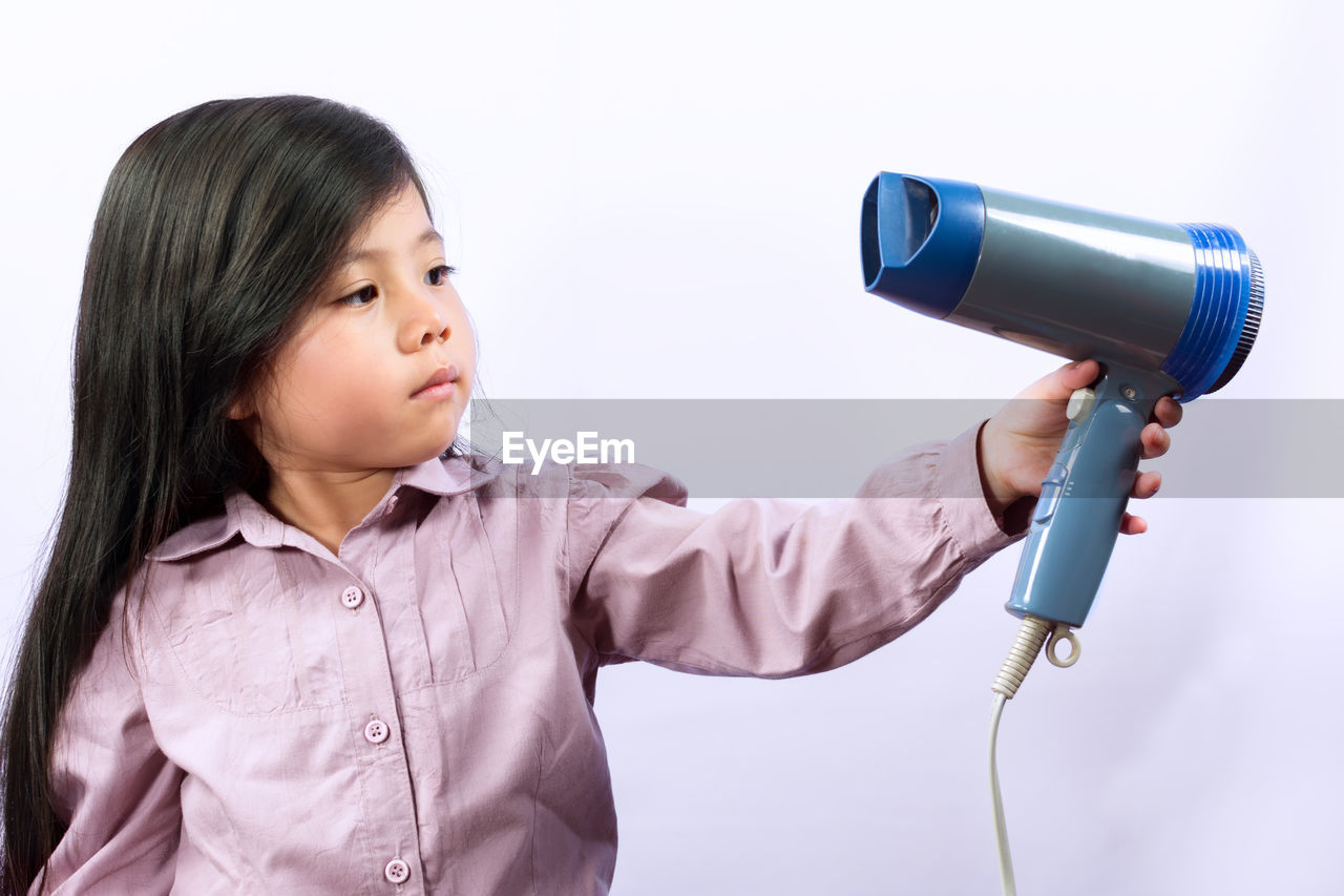 Close-up of cute girl holding hair dryer against white background