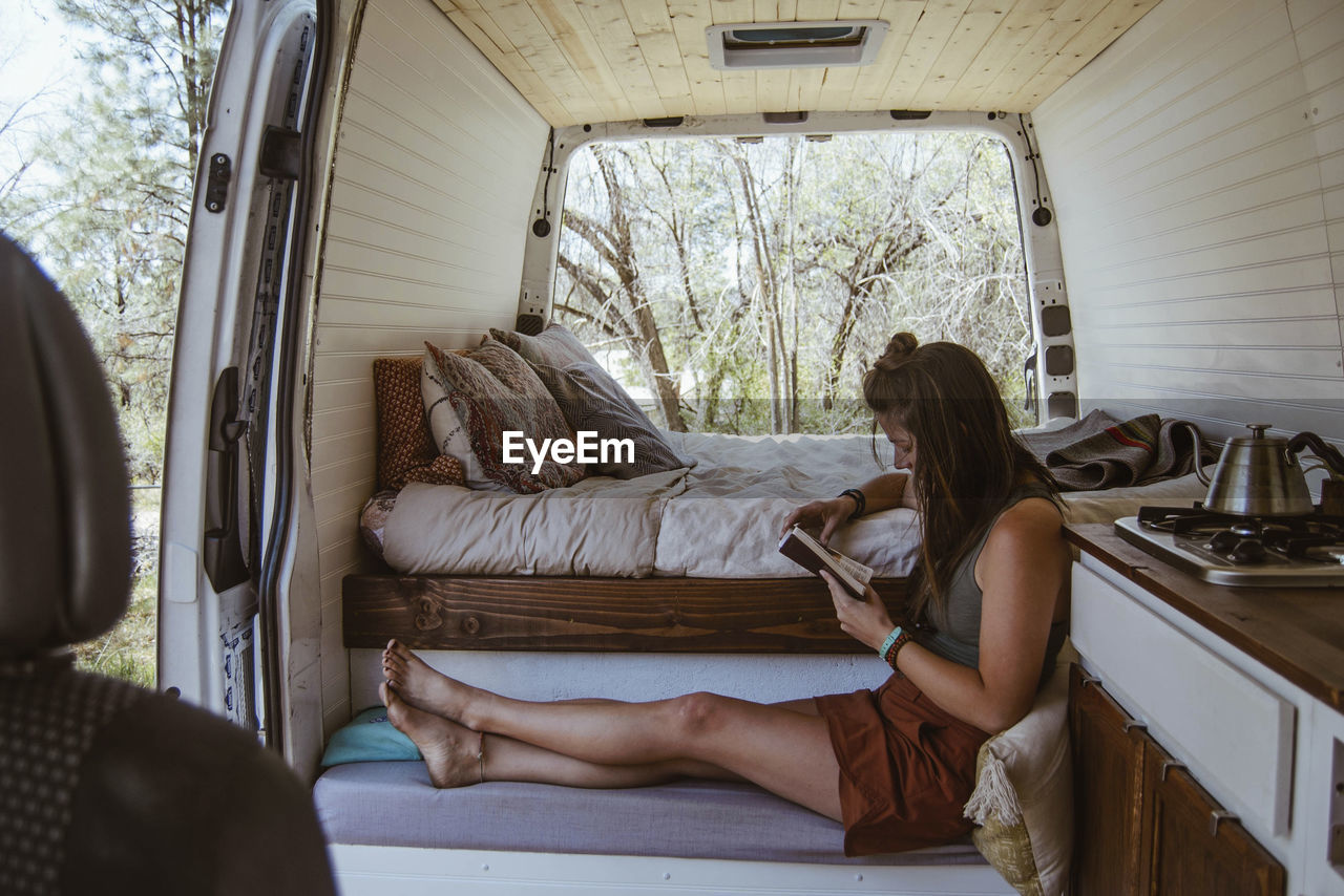 Side view of woman reading book while sitting on seat in motor home