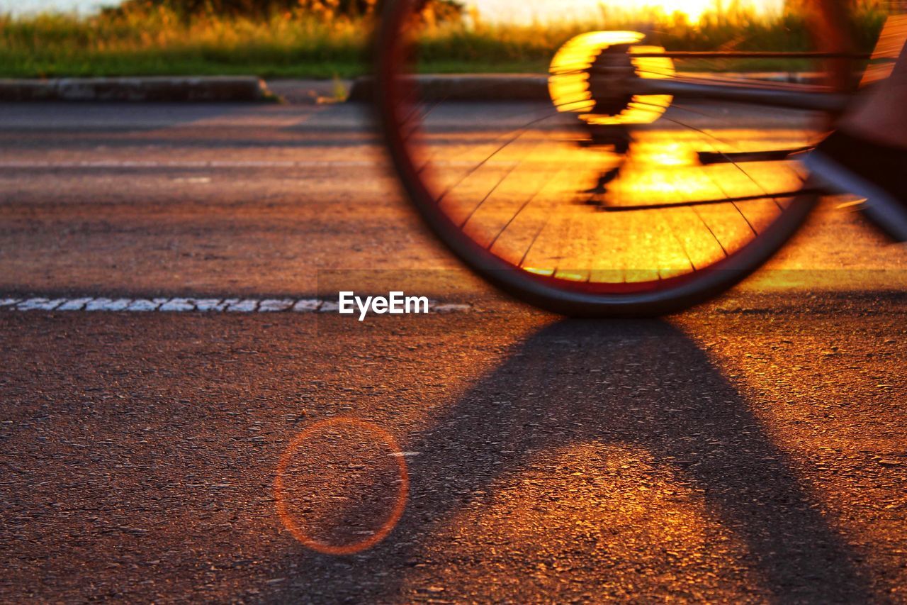 Low section of person riding bicycle on road during sunset