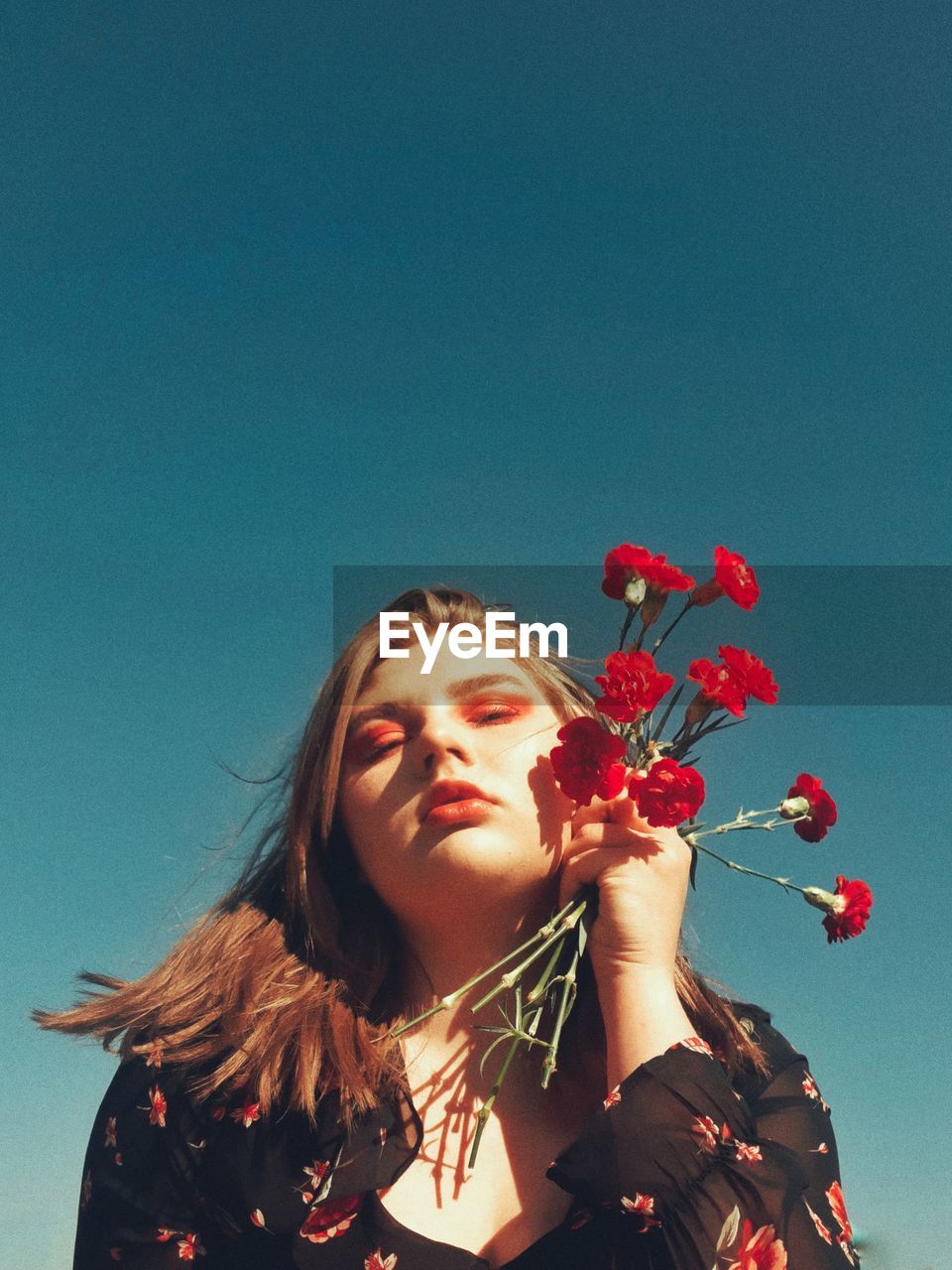 Portrait of young woman with red flowers against blue sky