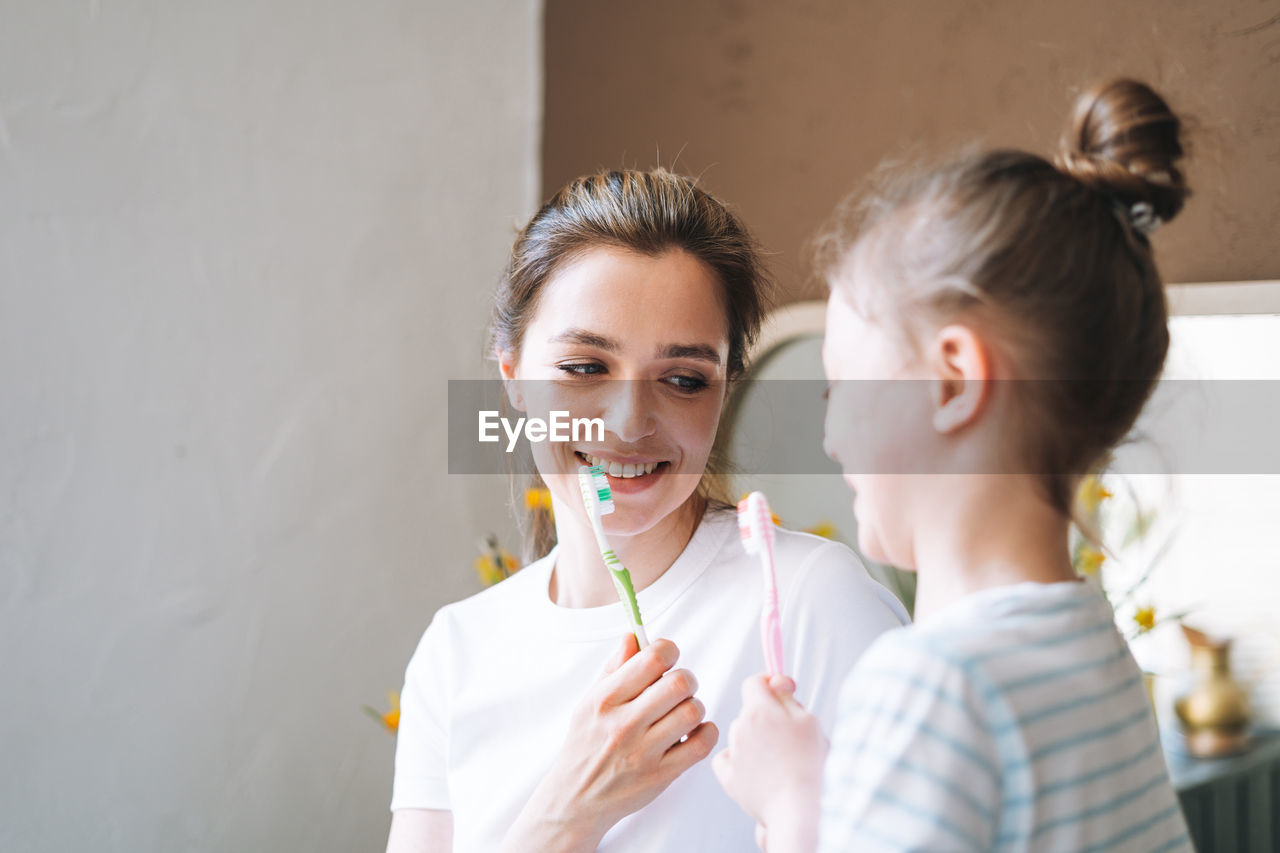 Young mother woman with little tween girl daughter in pajamas brushing their teeth at home