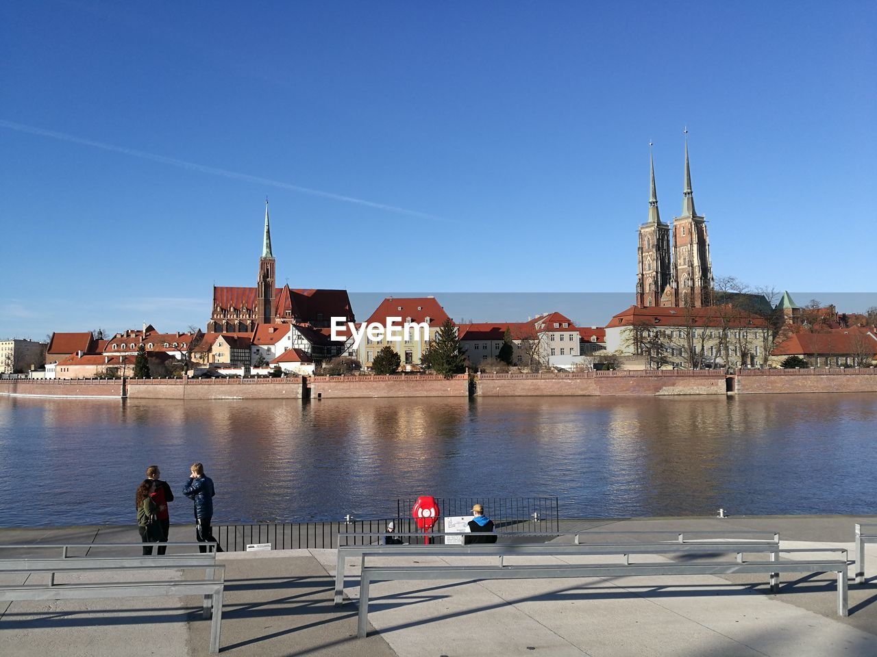 PEOPLE IN RIVER BY BUILDINGS AGAINST CLEAR SKY