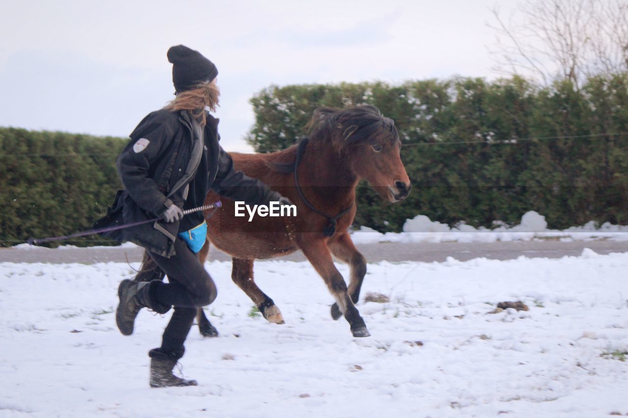 Woman running with horse against trees and sky